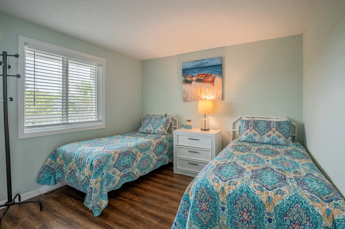 A twin bedroom with two beds dressed in patterned bedding, a bedside lamp, and cheerful wall art. The bright, airy setting is perfect for children or young explorers, with a layout that encourages both rest and conversation.