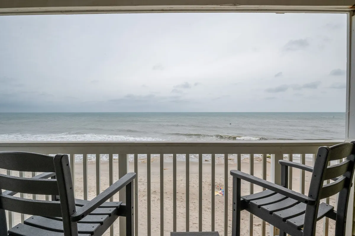 A private balcony overlooking the ocean, furnished with comfortable chairs. The scene captures the tranquil view of the waves and sandy beach, suggesting a peaceful spot to relax, read, or share a drink while enjoying the sights and sounds of the coast.