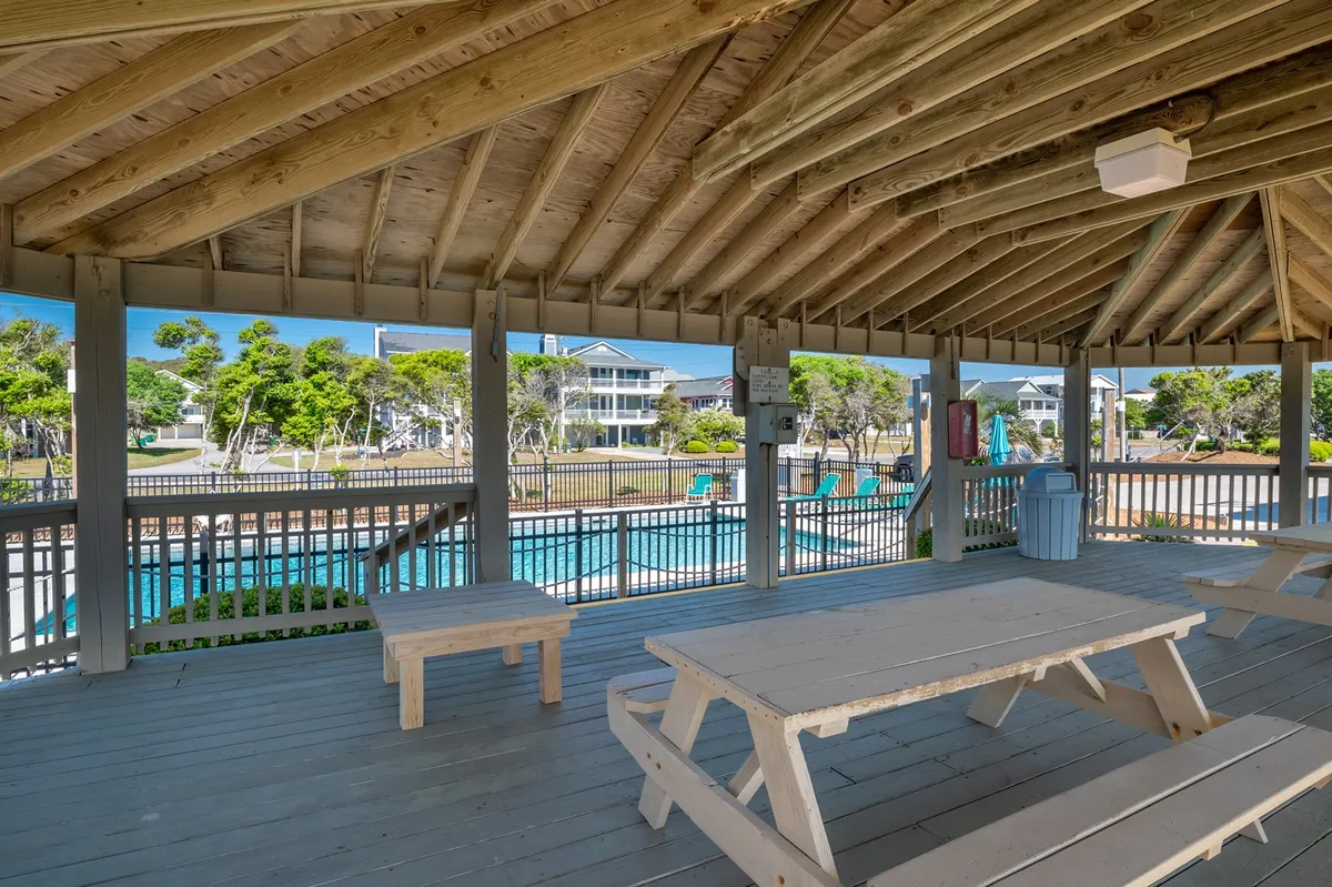 A covered picnic area with a sturdy wooden table and direct views of the pool, ideal for family meals, social gatherings, or relaxed outdoor dining amidst the resort atmosphere.