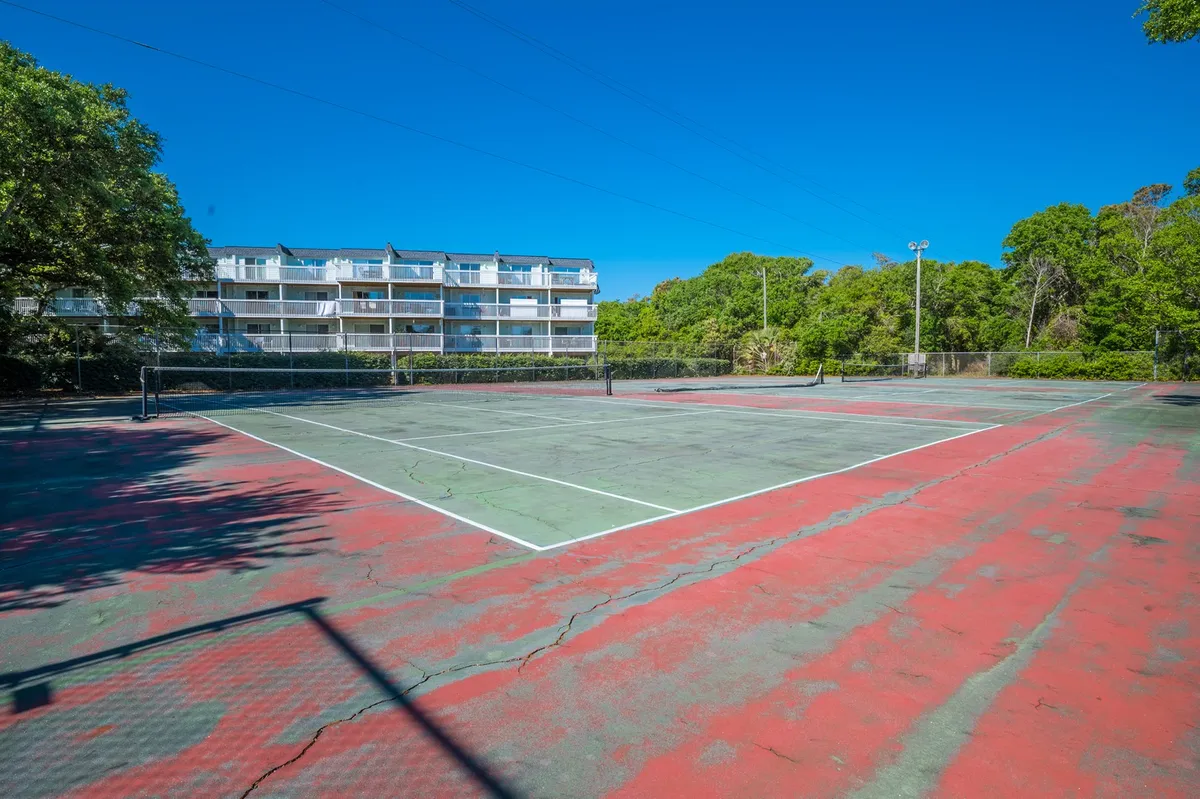 A well-maintained tennis court bordered by greenery and a backdrop of residential buildings. The court offers space for energetic matches, casual rallies, or learning the game together. The vibrant, open setting reinforces the active and engaging mood of the resort.