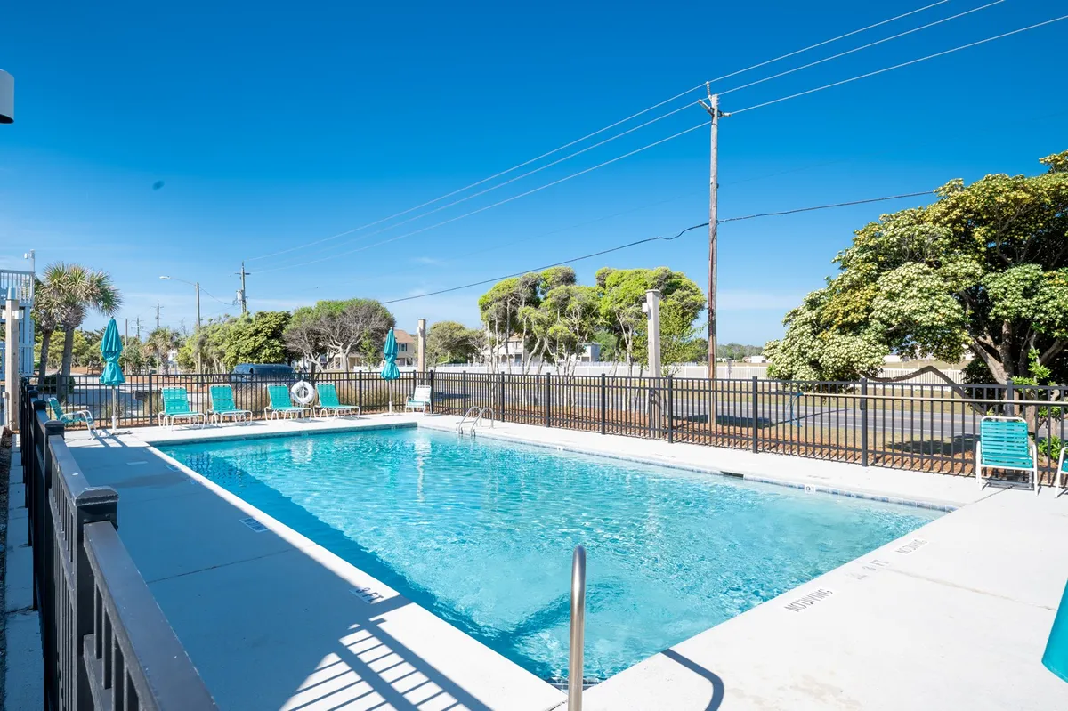 A sunlit outdoor swimming pool surrounded by lush greenery and several comfortable lounge chairs, inviting guests to swim, sunbathe, or relax by the water. The atmosphere is vibrant yet peaceful, perfect for family fun or quiet relaxation.