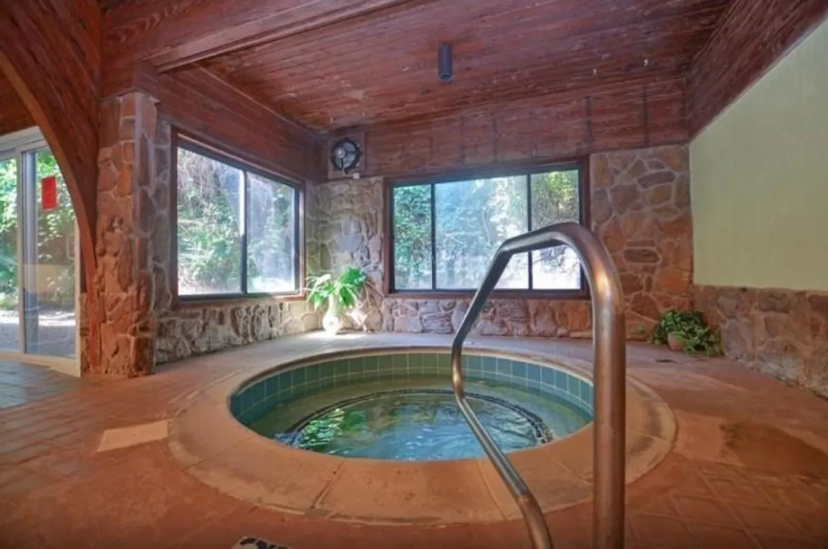 A tranquil interior spa area with a large soaking tub, surrounded by windows that let in natural light and greenery from outside. The space exudes calm and is ideal for wellness routines, relaxation, and intimate social moments.