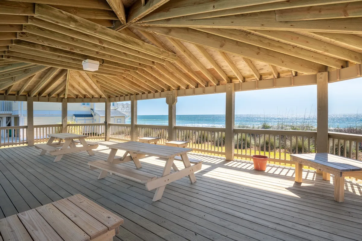 A relaxed, open-air picnic area with wooden tables and unobstructed views of the sea. The setting is ideal for group meals or watching sunsets, encapsulating the spirit of shared experiences and outdoor enjoyment.