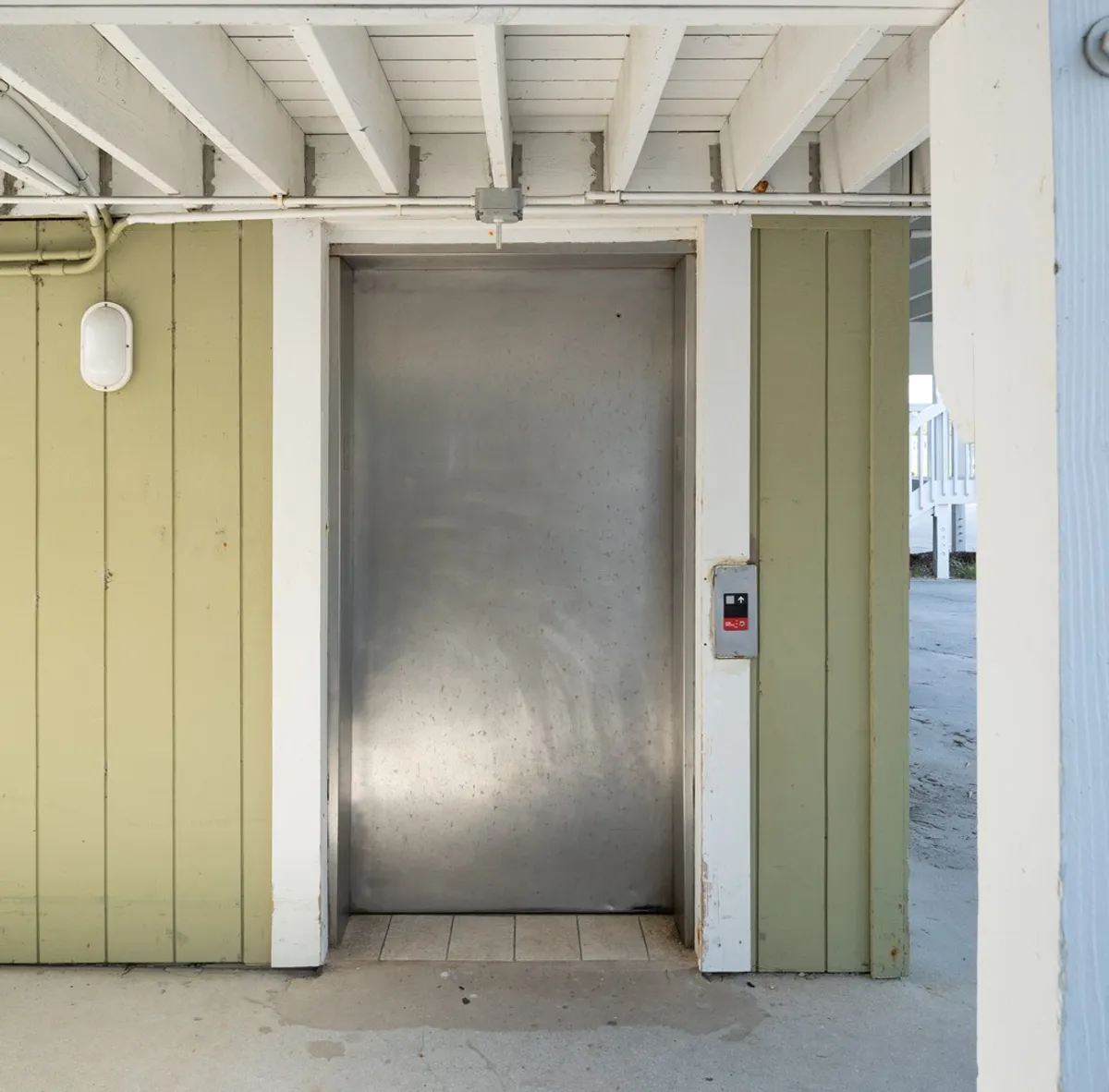 This image shows a close-up of the building's elevator with a green wall and visible control panel, indicating accessibility to upper floors. The scene is neutral, focusing on the functional aspect of elevator use.