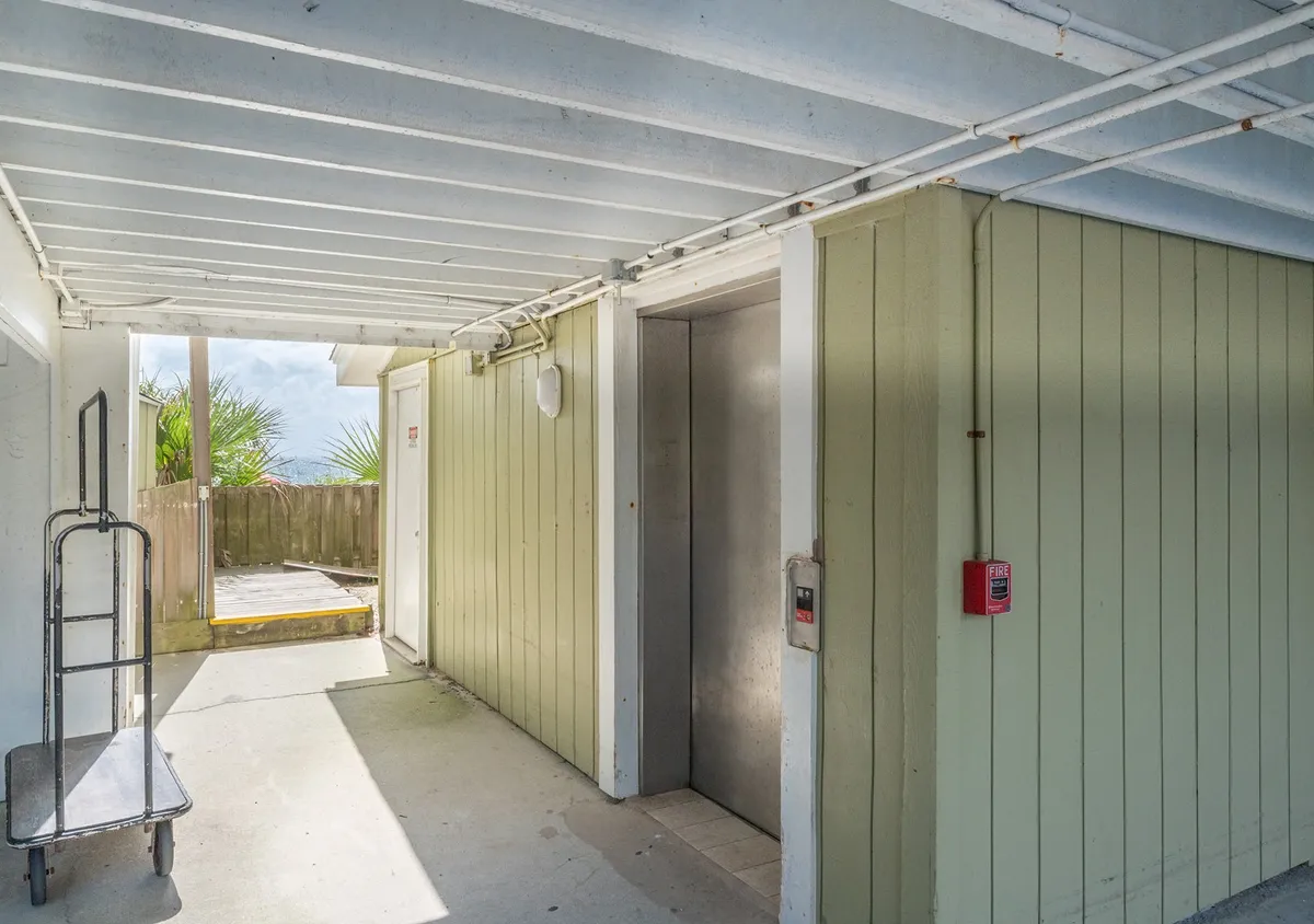 This interior image features the building's elevator, a luggage cart, and an exterior view through the window. The scene conveys a practical and welcoming atmosphere as guests arrive and move their belongings, highlighting the convenience of elevator access.